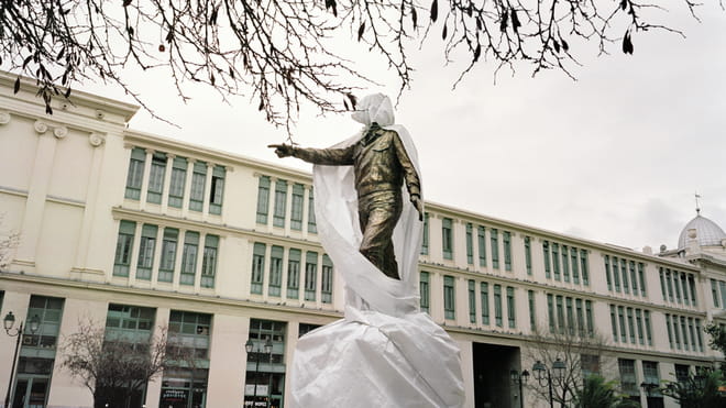 A half-covered statue being restored in Athens in front of a government building. 
